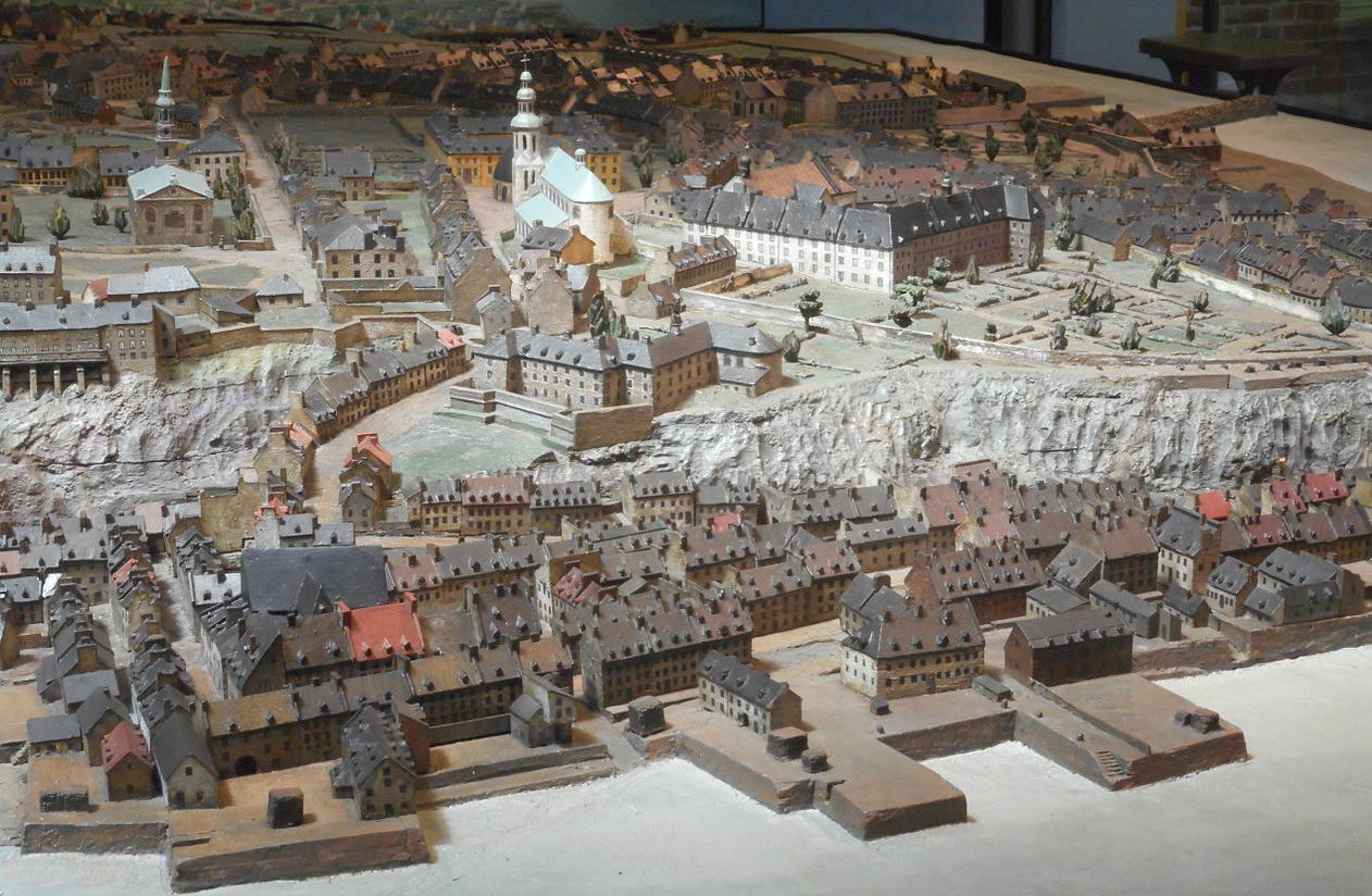 Photo of a scale model of an 18th century city. In the foreground are
    some docks along a river and the lower town containing many row-houses.
    Towering above the lower town on top of a large bluff is the upper town,
    surrounded by stone walls. Two large churches feature prominently. In the
    background, farmland can be seen stretching away to the horizon.