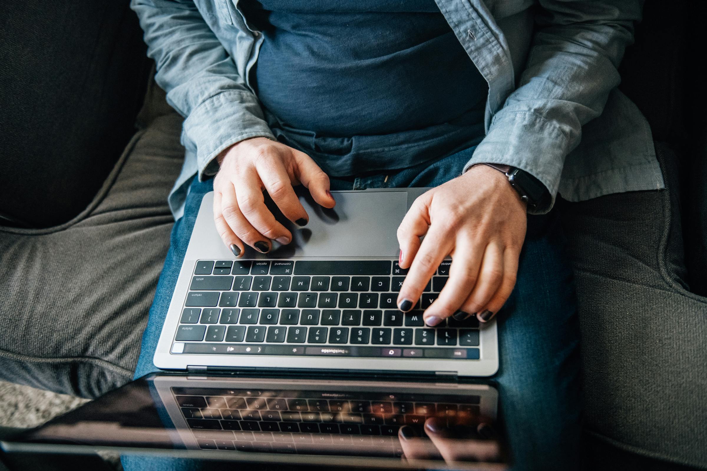 Hands typing on an open laptop on top of a person's lap.