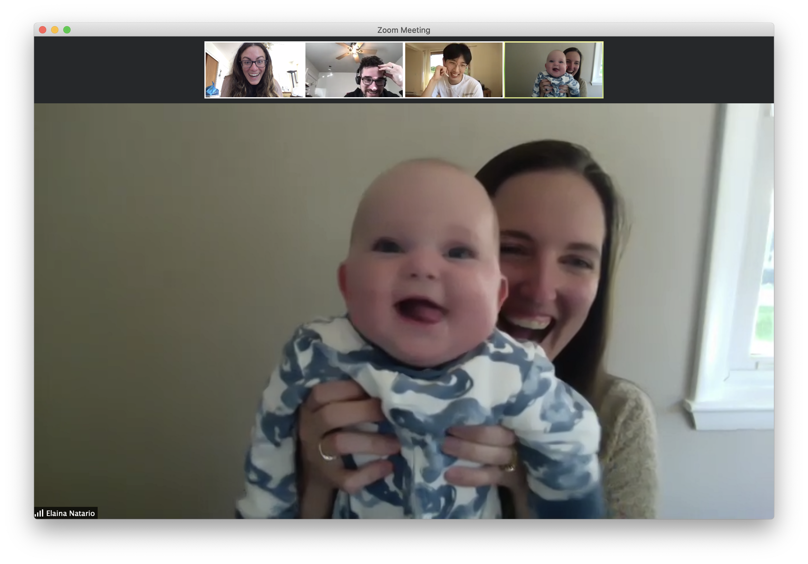 A screen capture of a video meeting on Zoom. There are four small screens at the top, each with a person making a funny face. The large central photo at the bottom is a woman smiling holding up a baby who is also smiling.